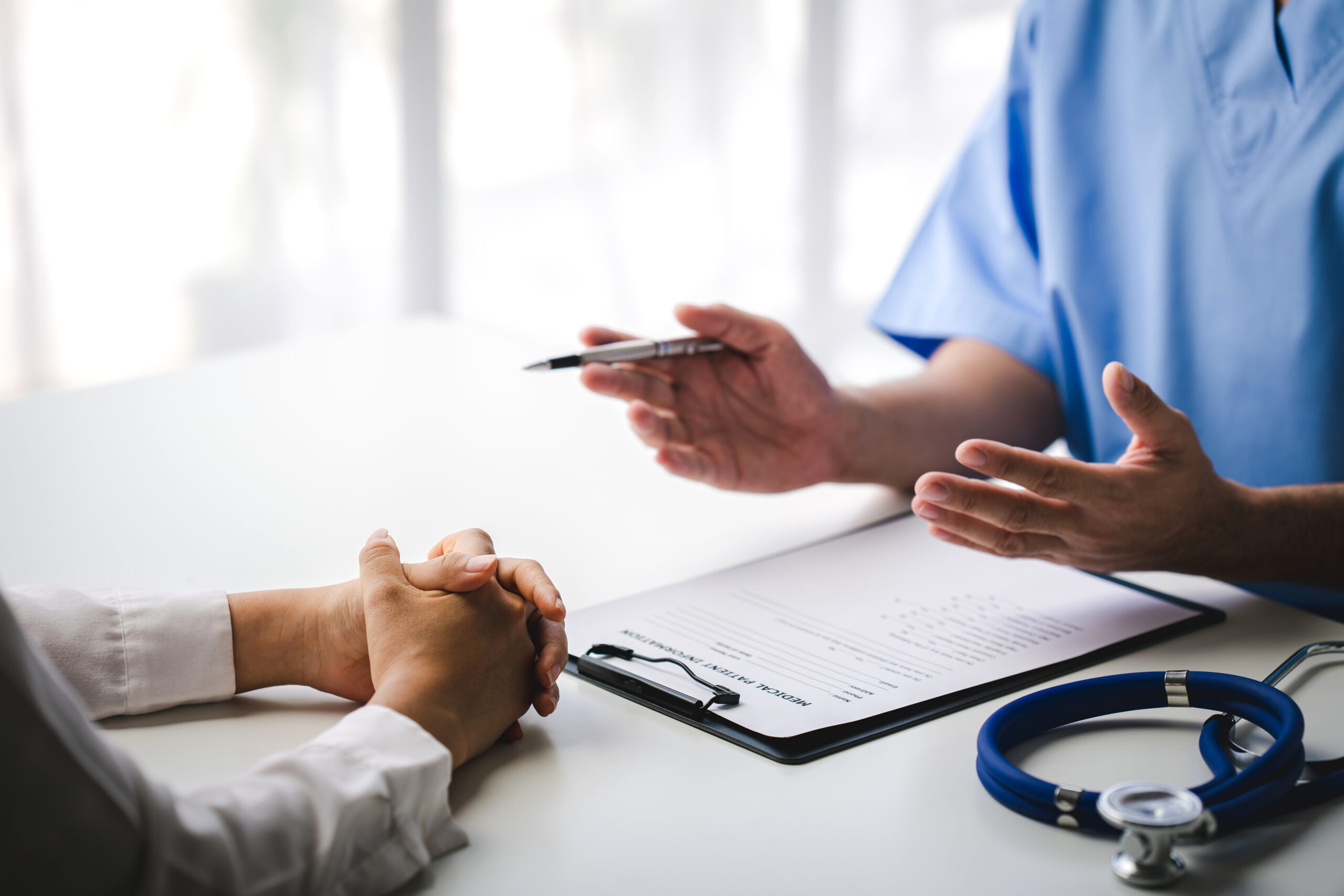 Image of the hands of a doctor sitting across the desk from a patient.