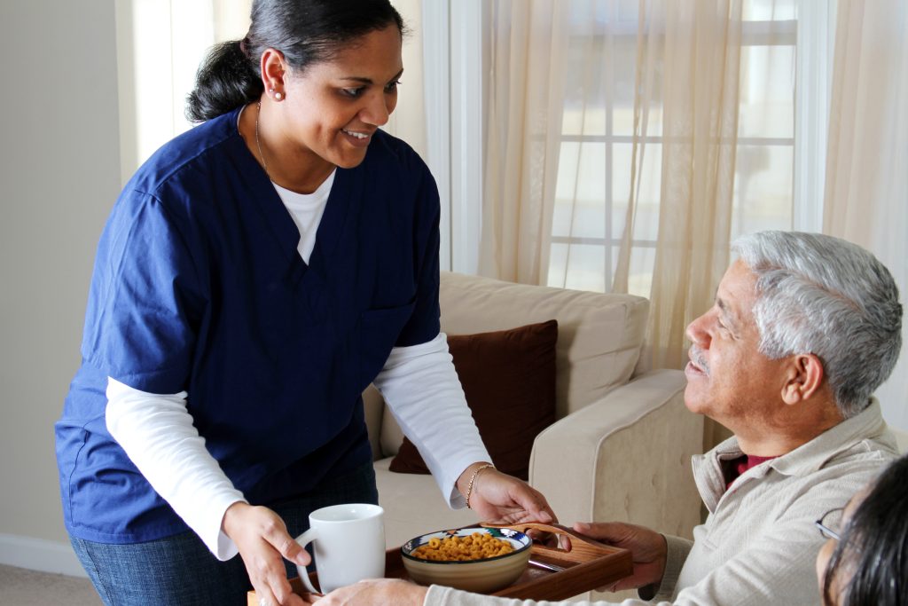 Care worker delivering food to elderly man.