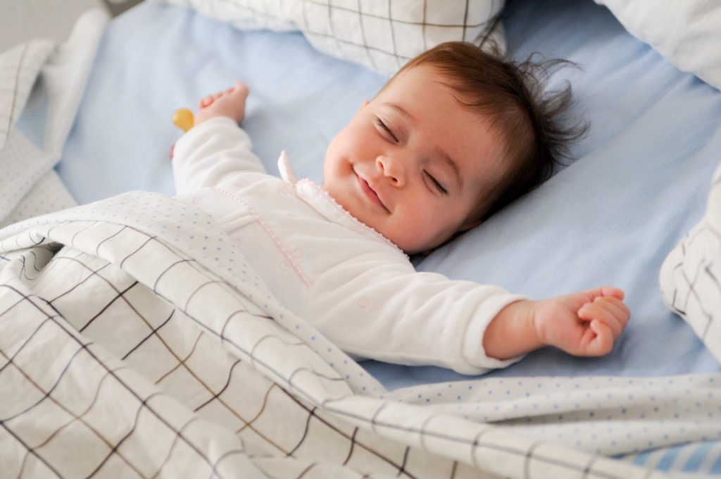 A smiling baby sleeping in a bed