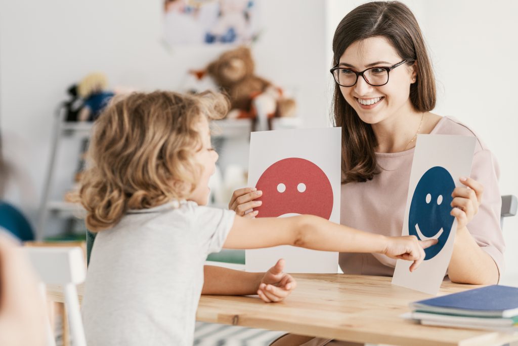 Child in counselling session with female being asked to point to a happy or sad face.