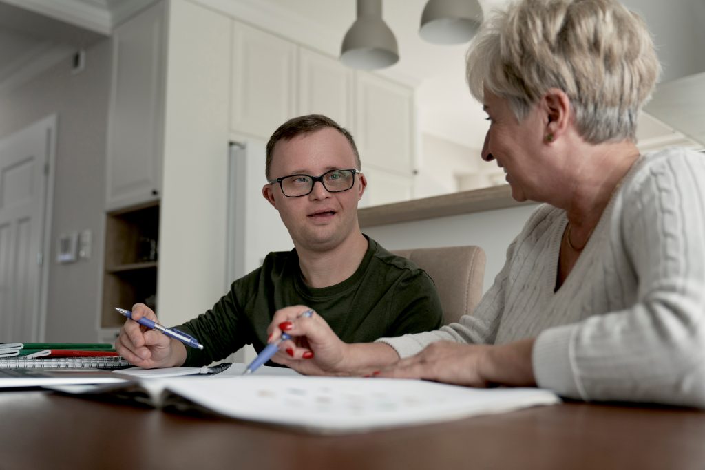 Mum helping young man with learning disabilities with college work at home.