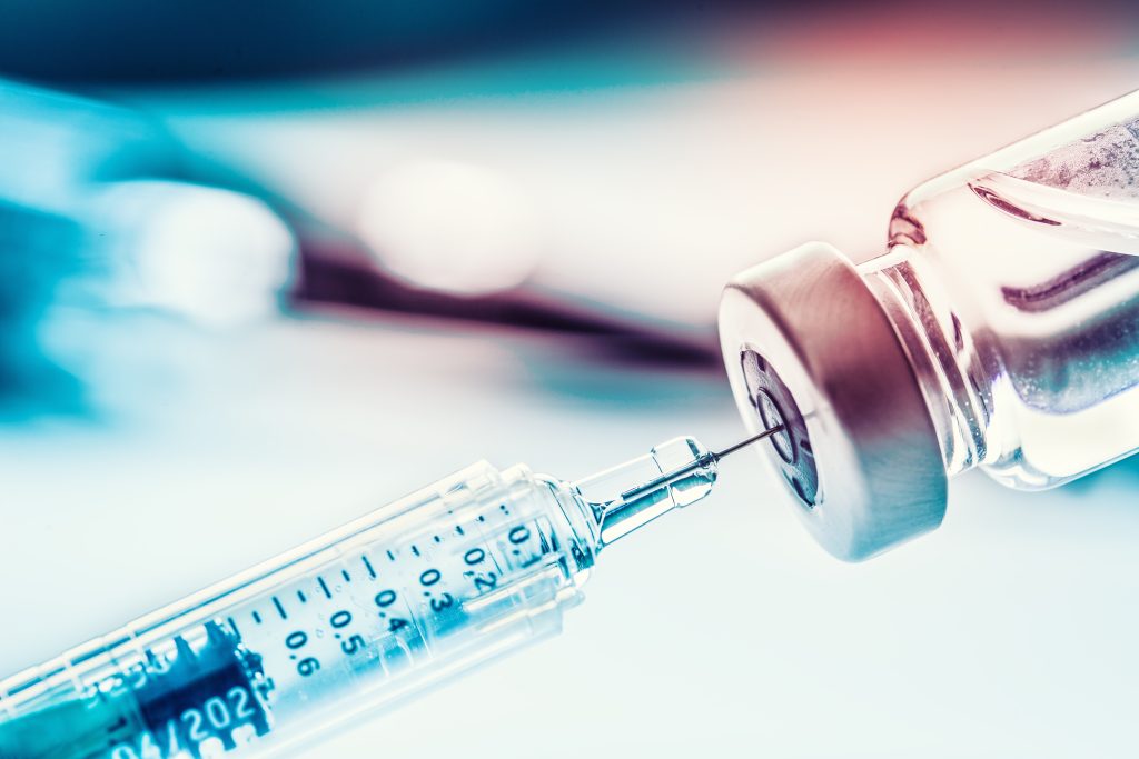 Close-up of medical syringe inside vaccine bottle.