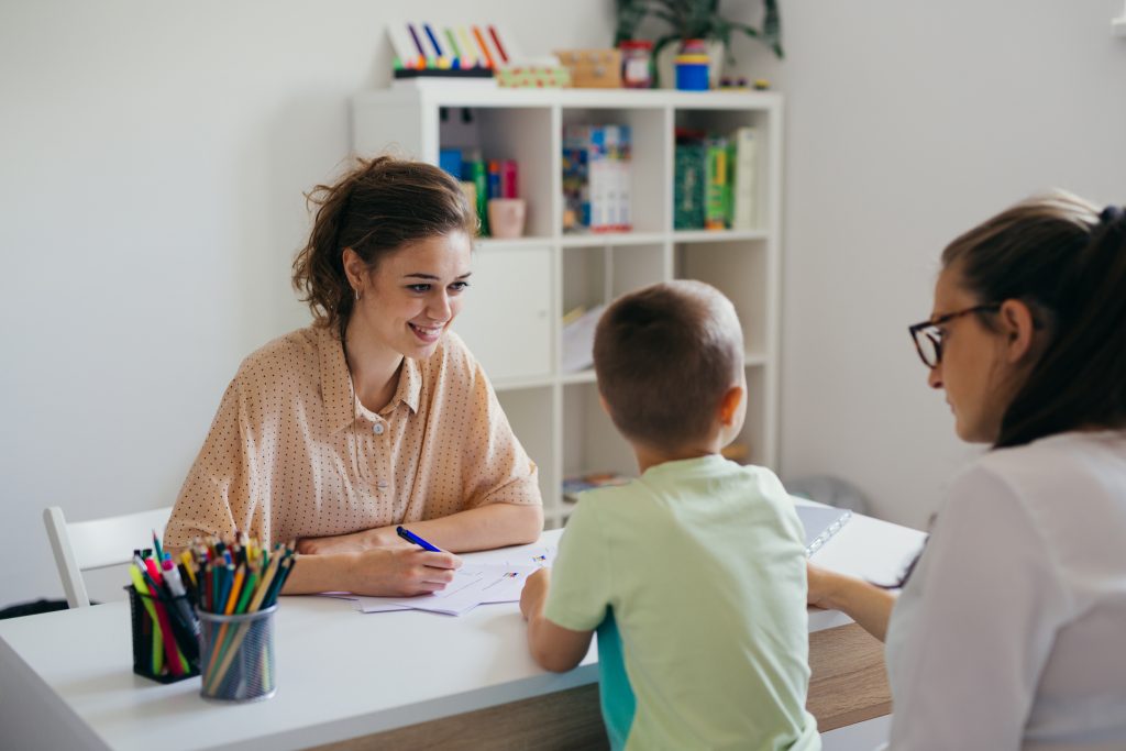 Child and parent at a table colouring with a health practitioner looking on.