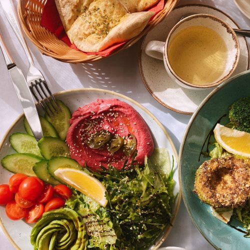 A vibrant vegan brunch featuring hummus, fresh veggies, tea, and pita bread on a sunlit table.